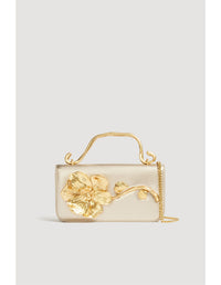 Aje Celeste Flower Clutch featuring a gold top handle and gold sculpted flower detail, photographed against a clean studio backdrop.